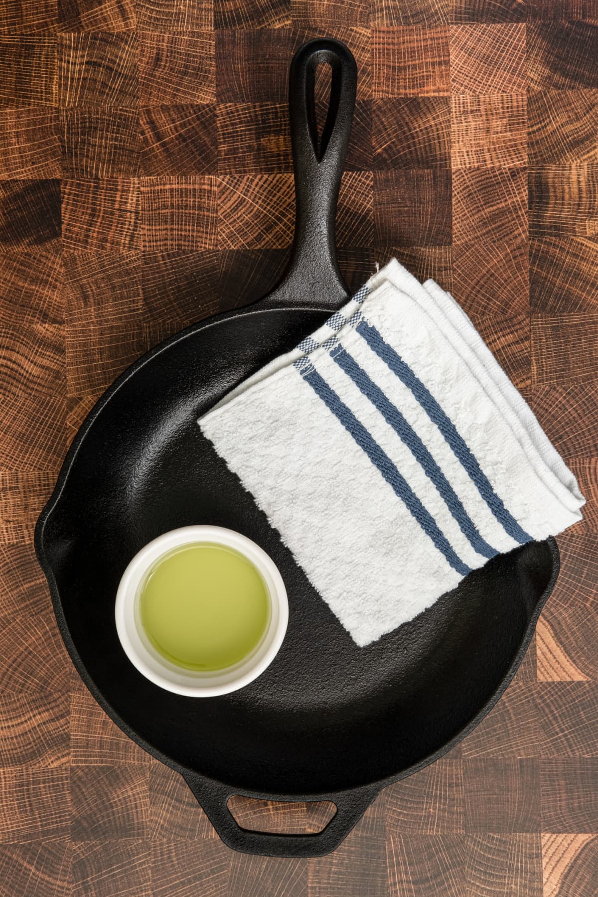 A cast-iron skillet with a cup of grapeseed oil and a towel on a brown surface