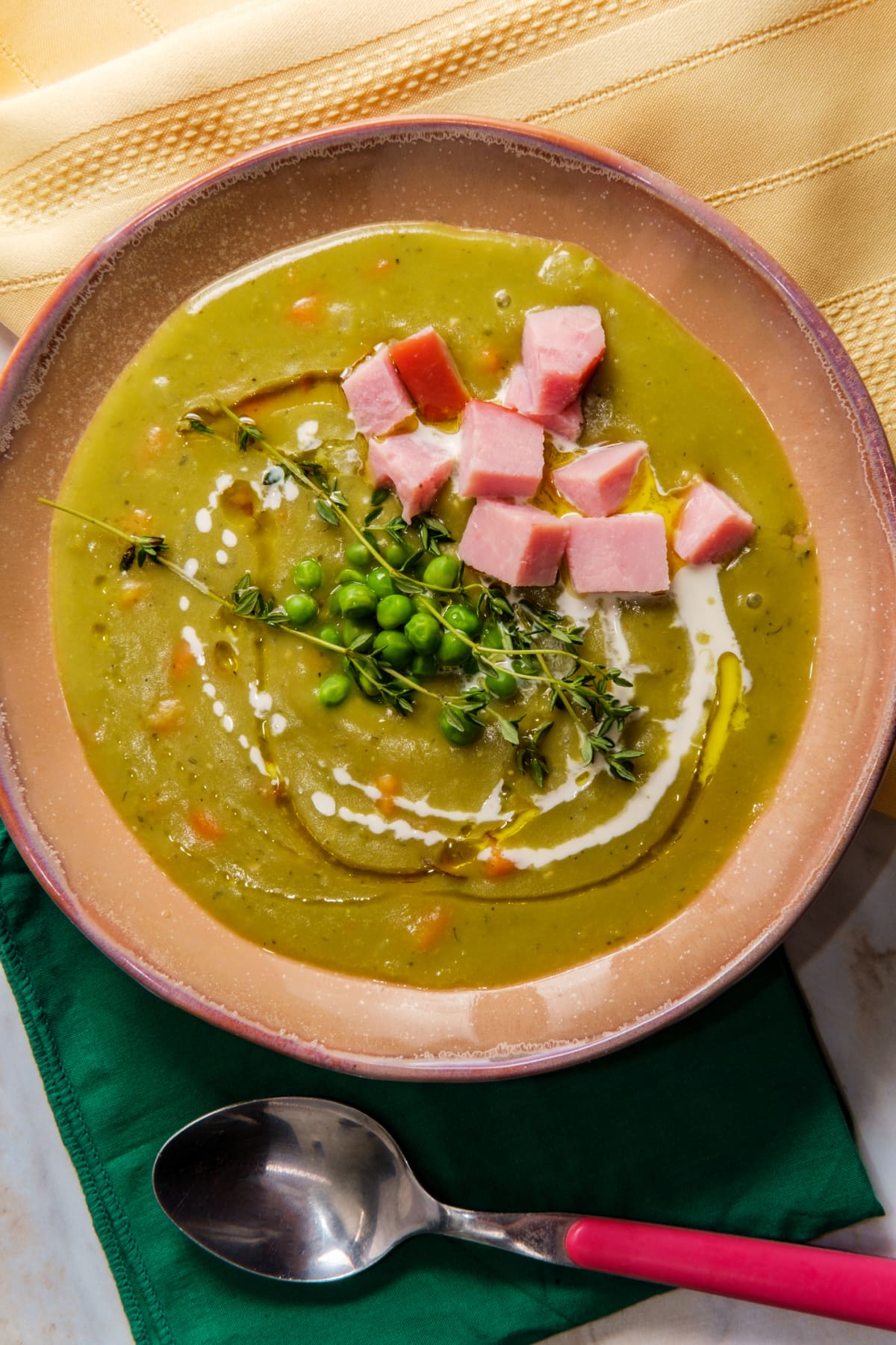 Bowl of split pea soup topped with peas, ham and herbs
