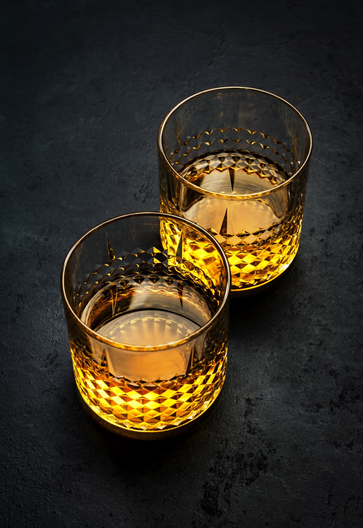 Two glasses of bourbon against black
