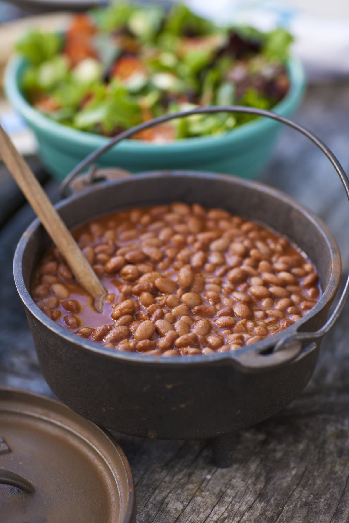 Baked beans in a dark pot with a wooden utensil