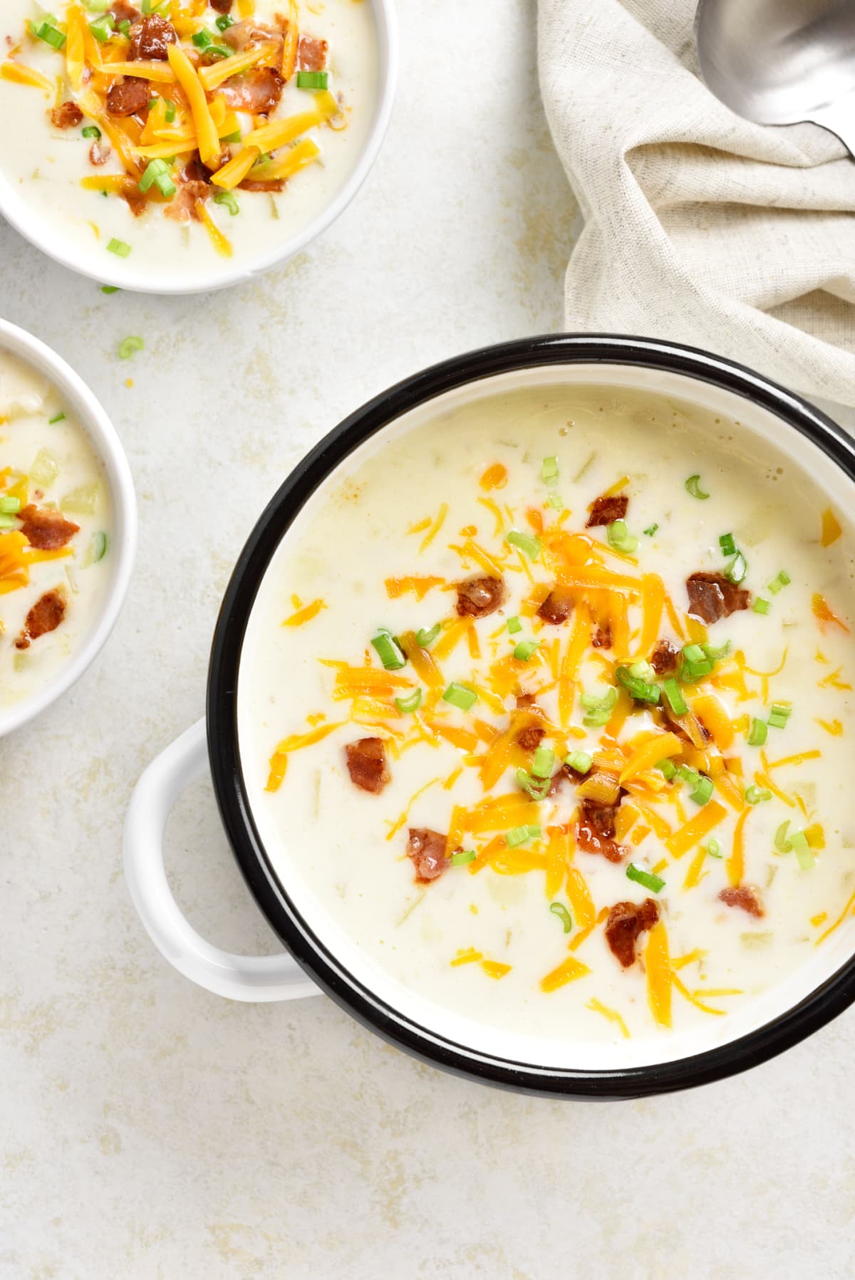Pot of potato soup topped with bacon, shredded cheddar, and green onions