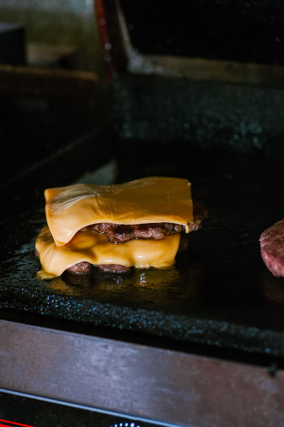 Double beef burgers with cheese on a plancha grill. Food preparing concept.