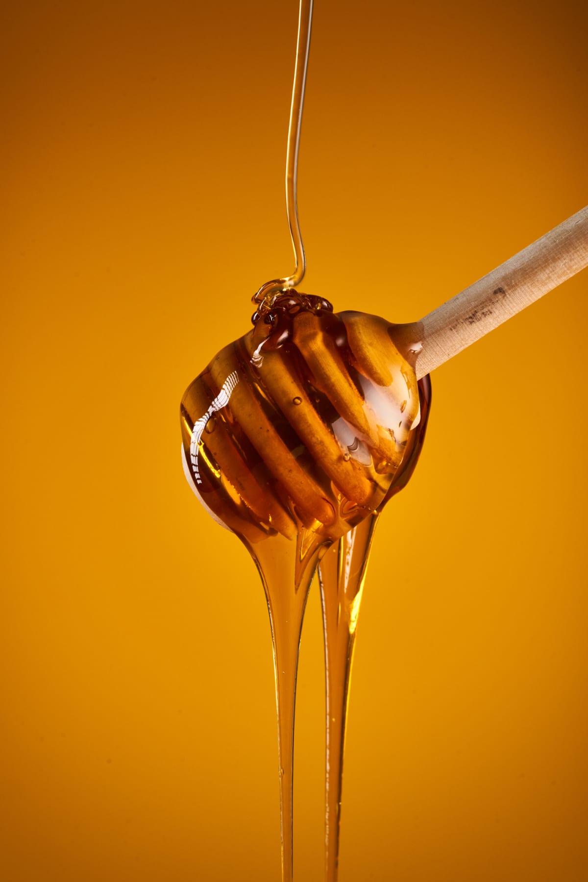 Closeup of honey dripping off a wooden dipper, isolated on yellow background