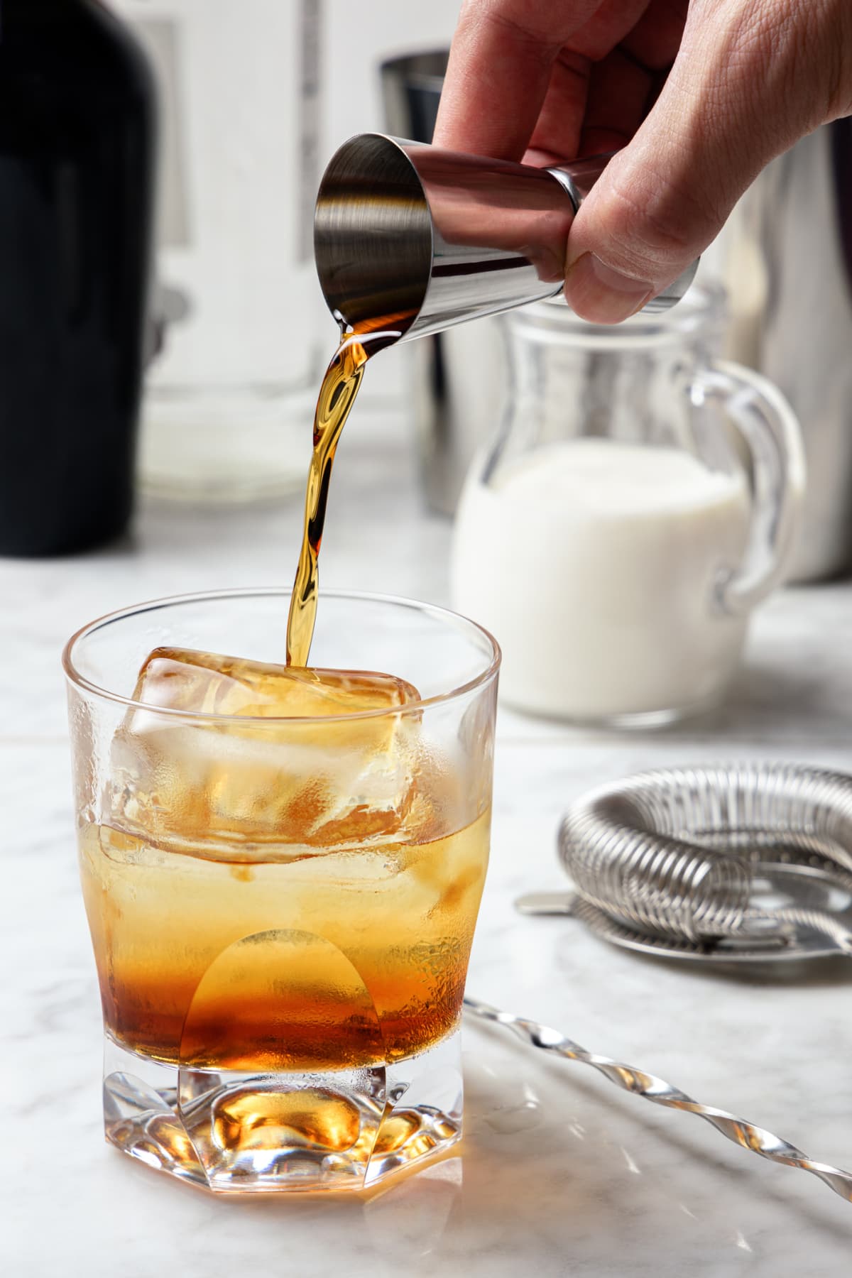 Man's hand pouring coffee liquor into a glass with ice. White Russian cocktail preparation