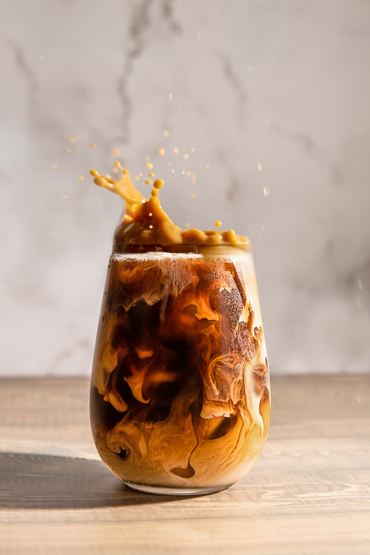 Iced coffee in a glass splashing out with drops on grey background