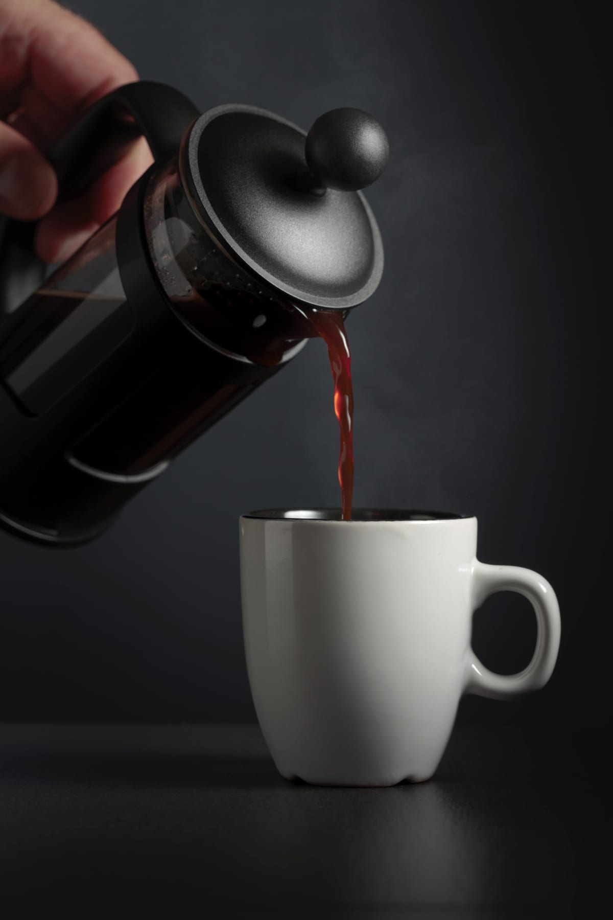 Pouring French press coffee into a cup on a black table.