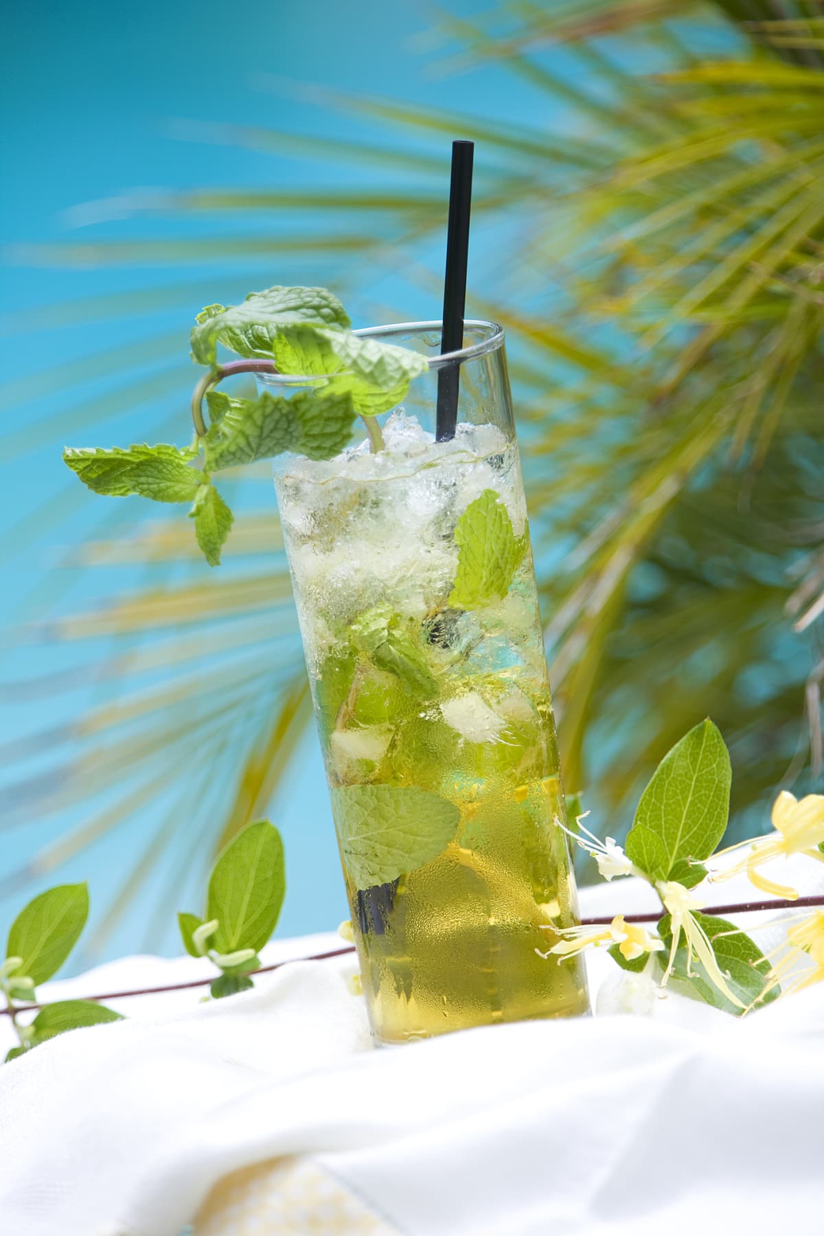 A mezcal and tequila cocktail with lime and mint garnish, paper straw, and abundant ice by a swimming pool