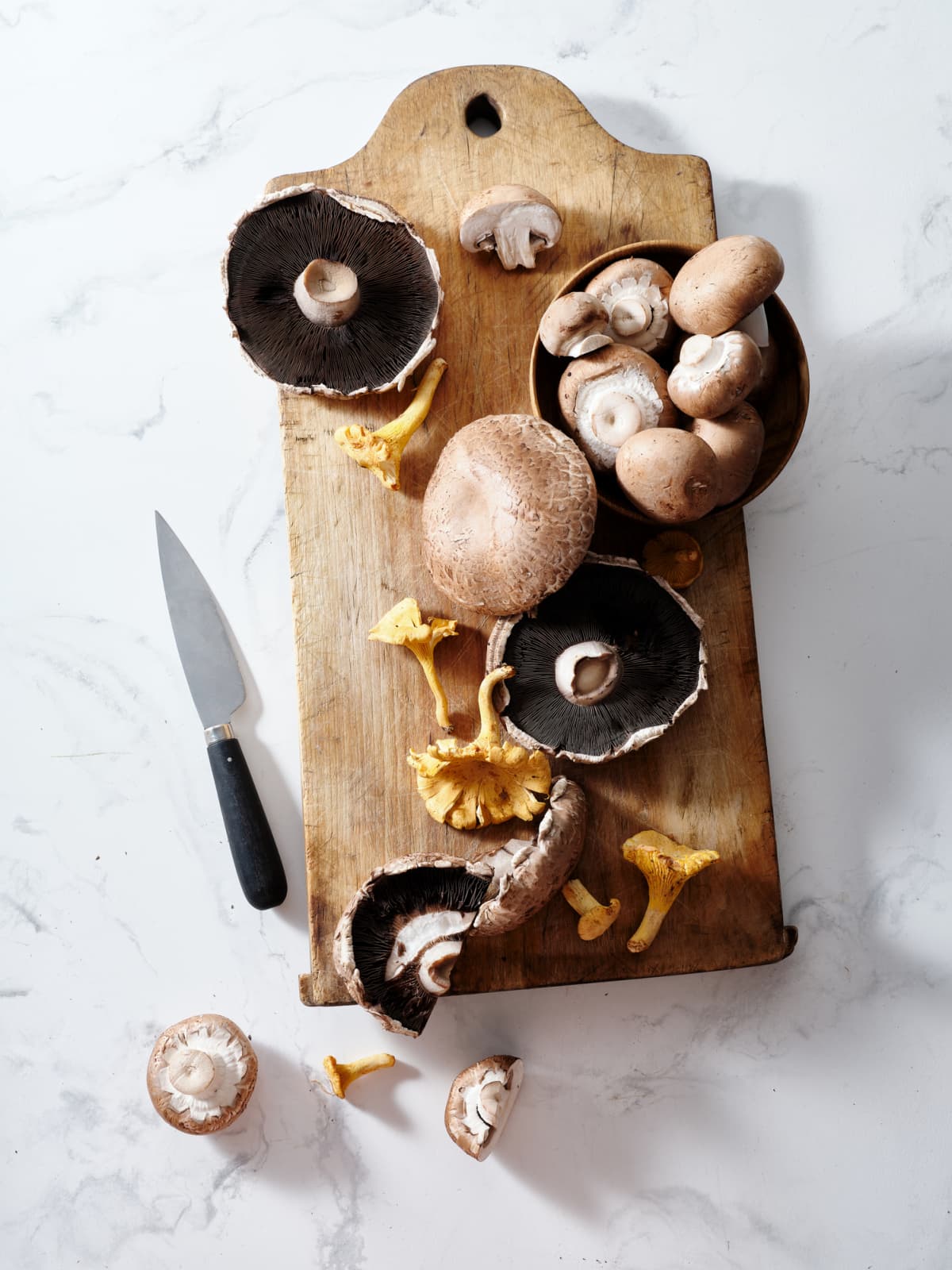 Various types of mushrooms on wooden cutting board with knife