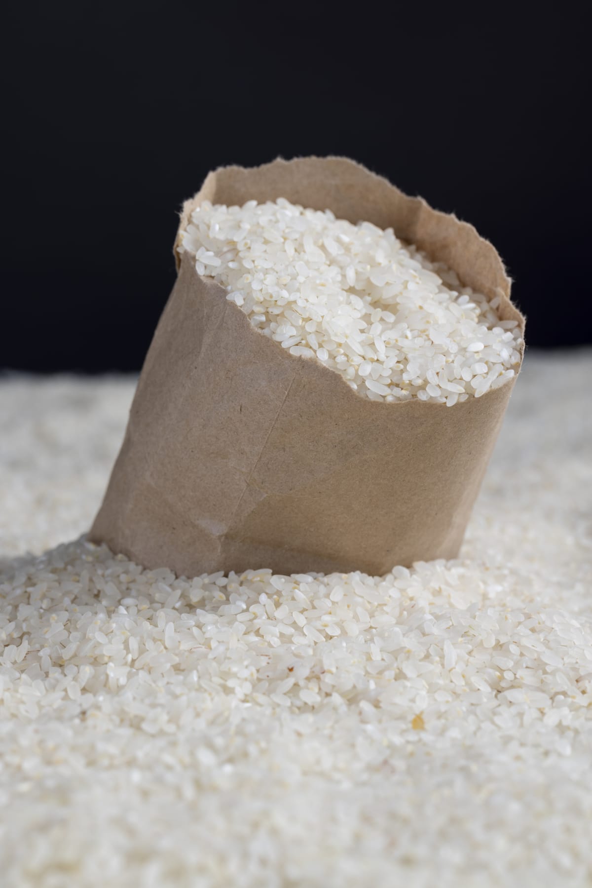 a pile of white rice in a paper bag and on the table, white uncooked rice grains in a paper bag on the table