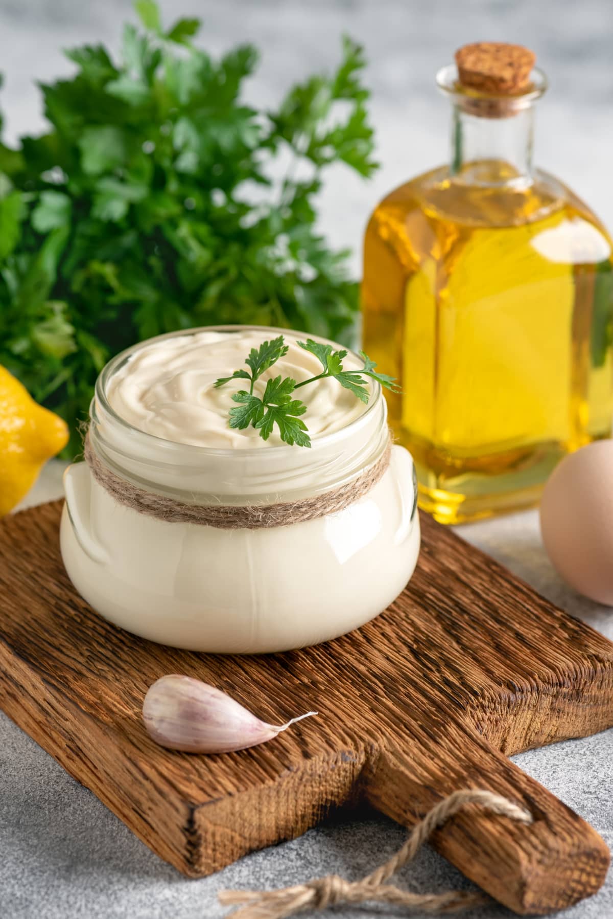 Jar of aioli on wooden platter with sprig of parsley