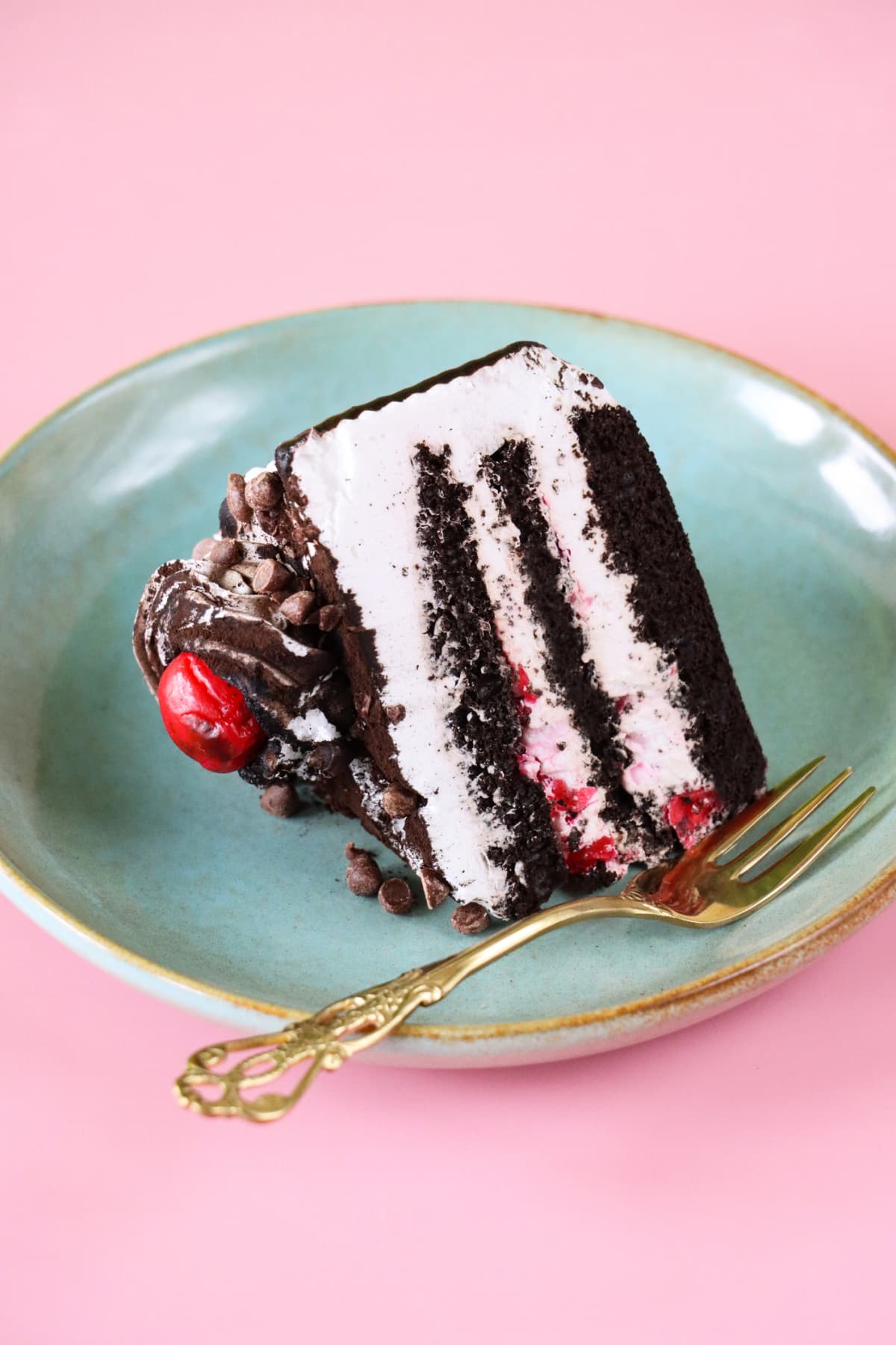 Slice of chocolate cake with white frosting and a cherry on a blue plate