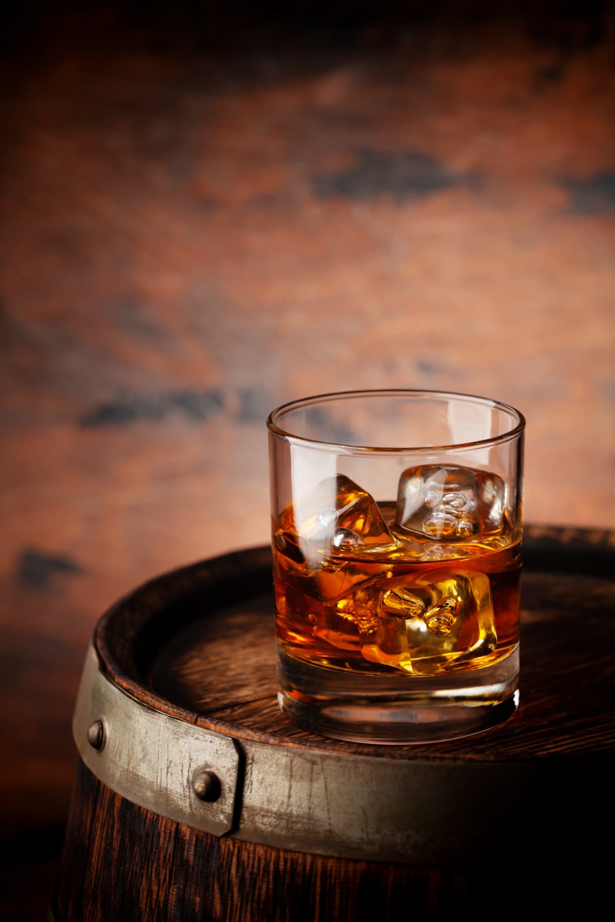 Glass of whiskey with ice cubes on barrel