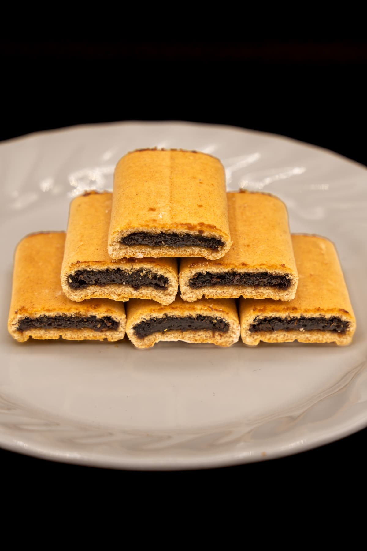 Fig Newtons on a white plate on a black background.