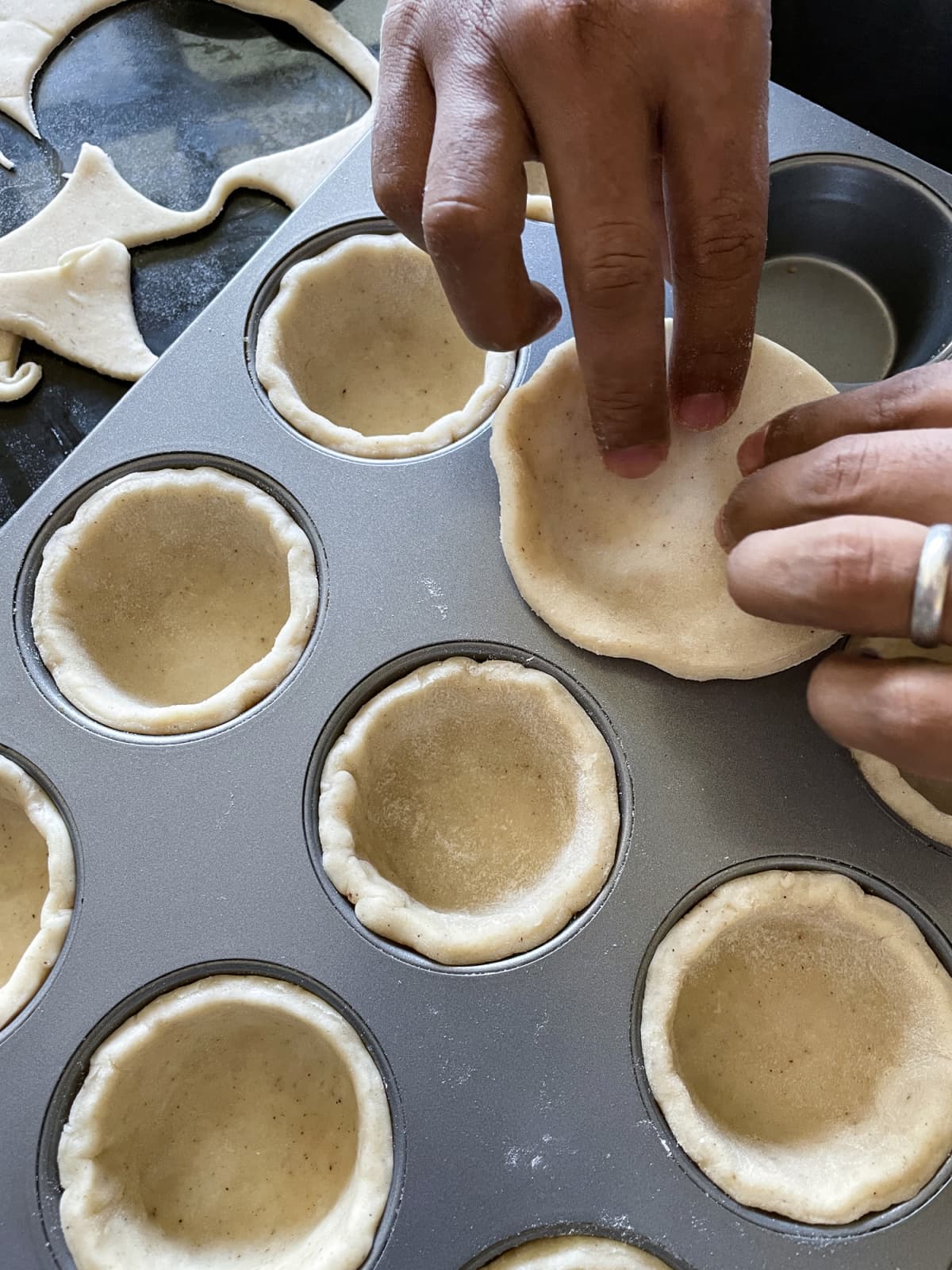 Hands placing pastry crust in a muffin tray