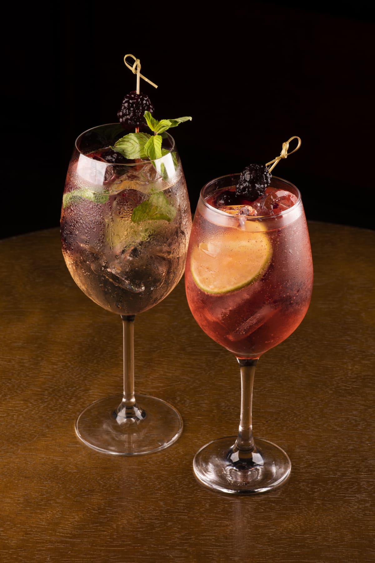 Two spritzes, one with mint and blackberry garnish, the other with orange peel and blackberry garnish