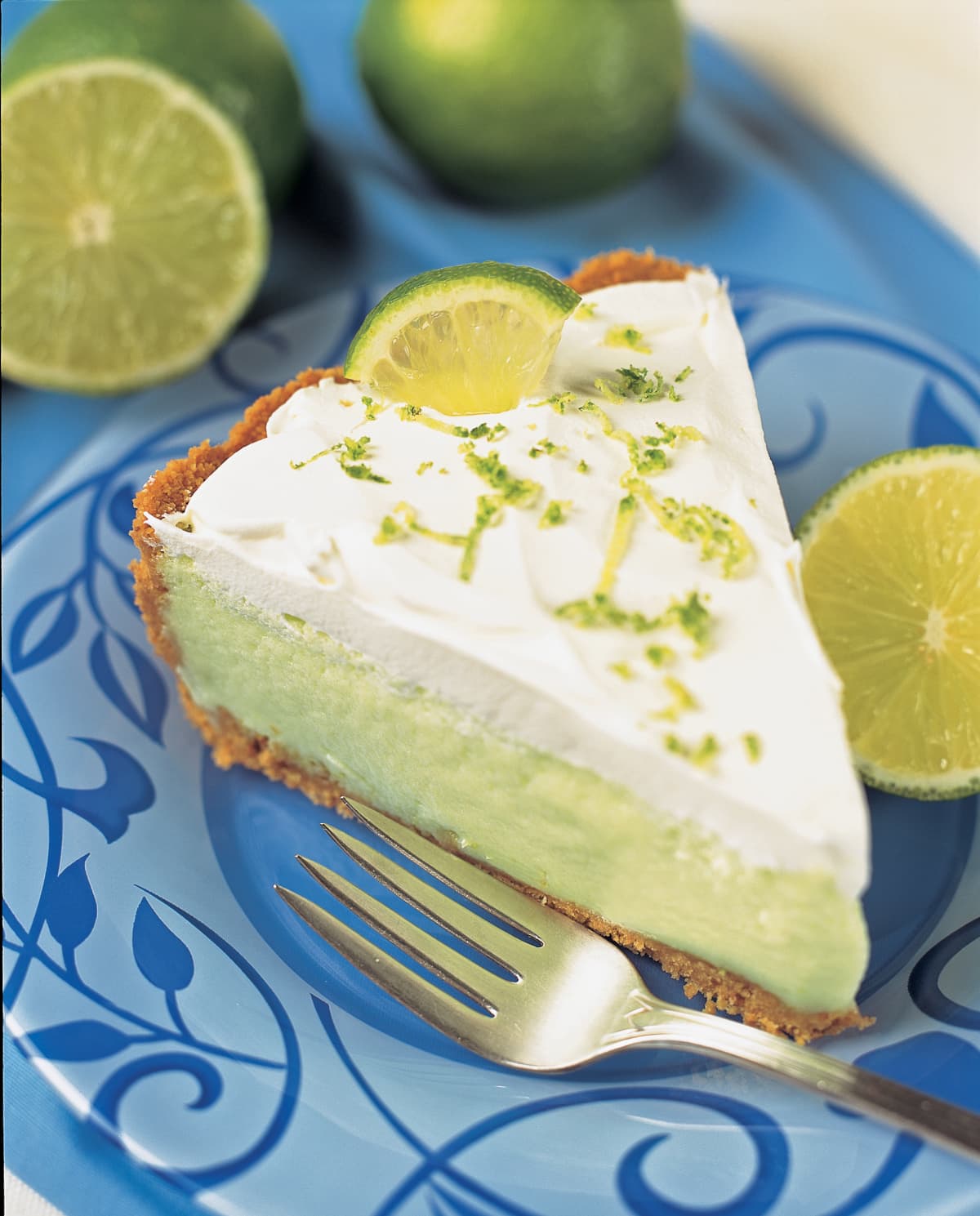 Key lime pie on a blue plate with fork and lime garnish