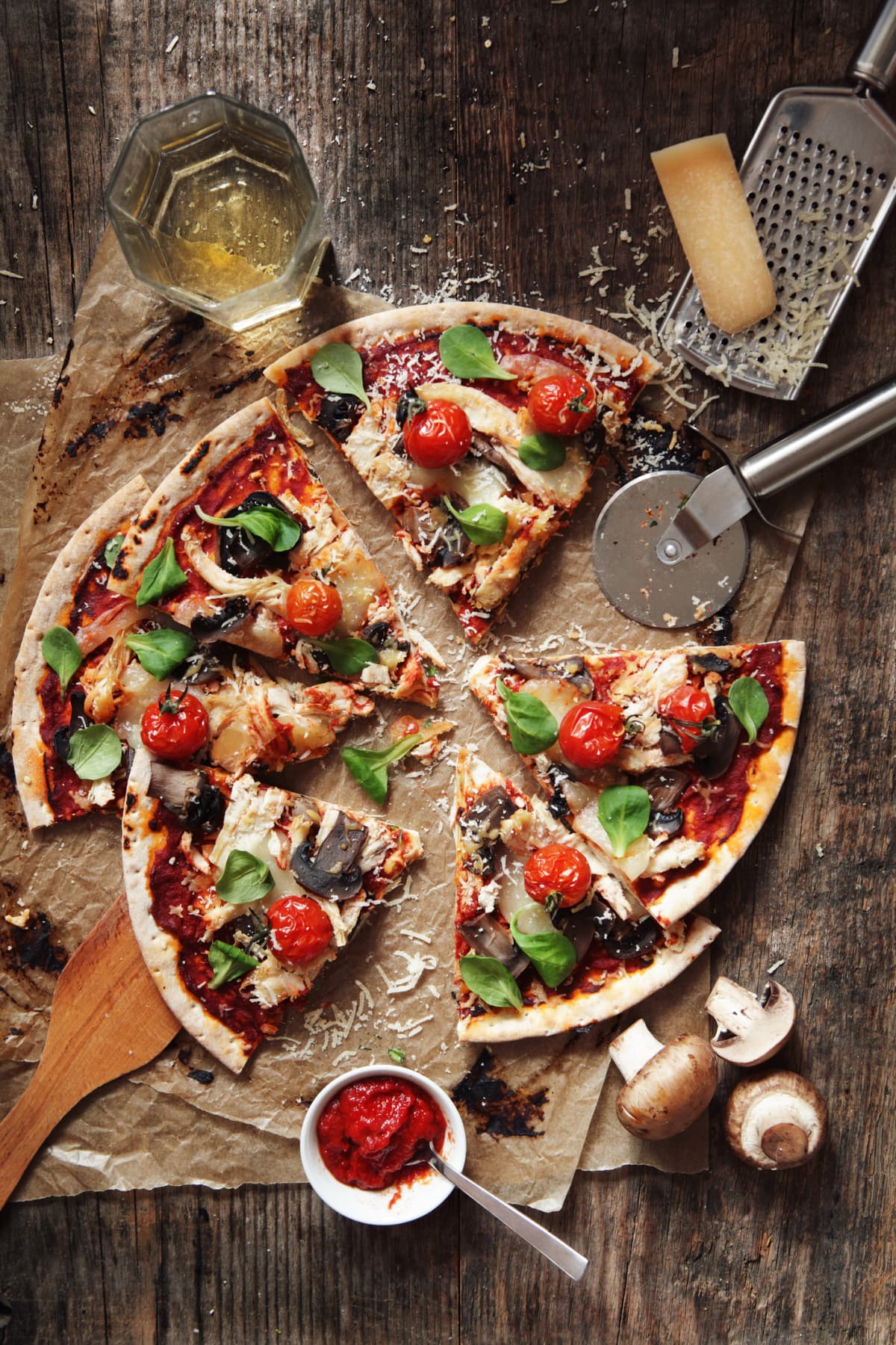 Pizza with tomatoes, spinach, and mushrooms cut into slices on wooden countertop