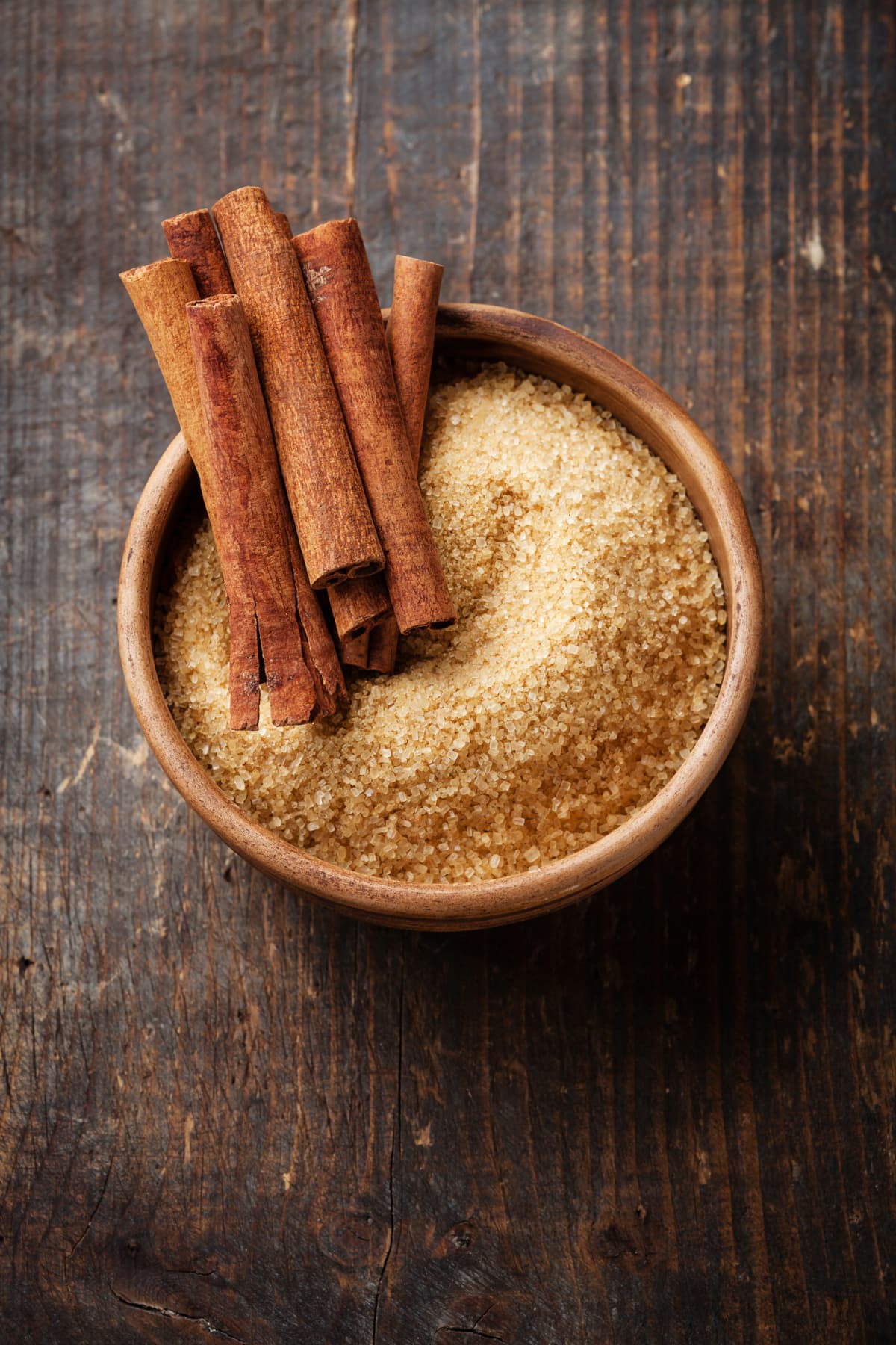 Wooden bowl of sugar with cinnamon sticks on top