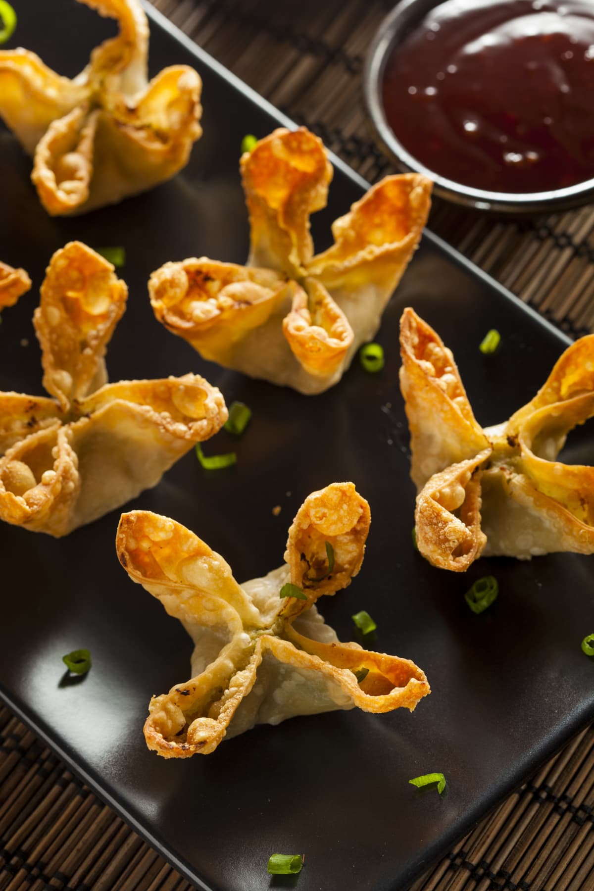 Fried crab rangoons on plate with chopped chives
