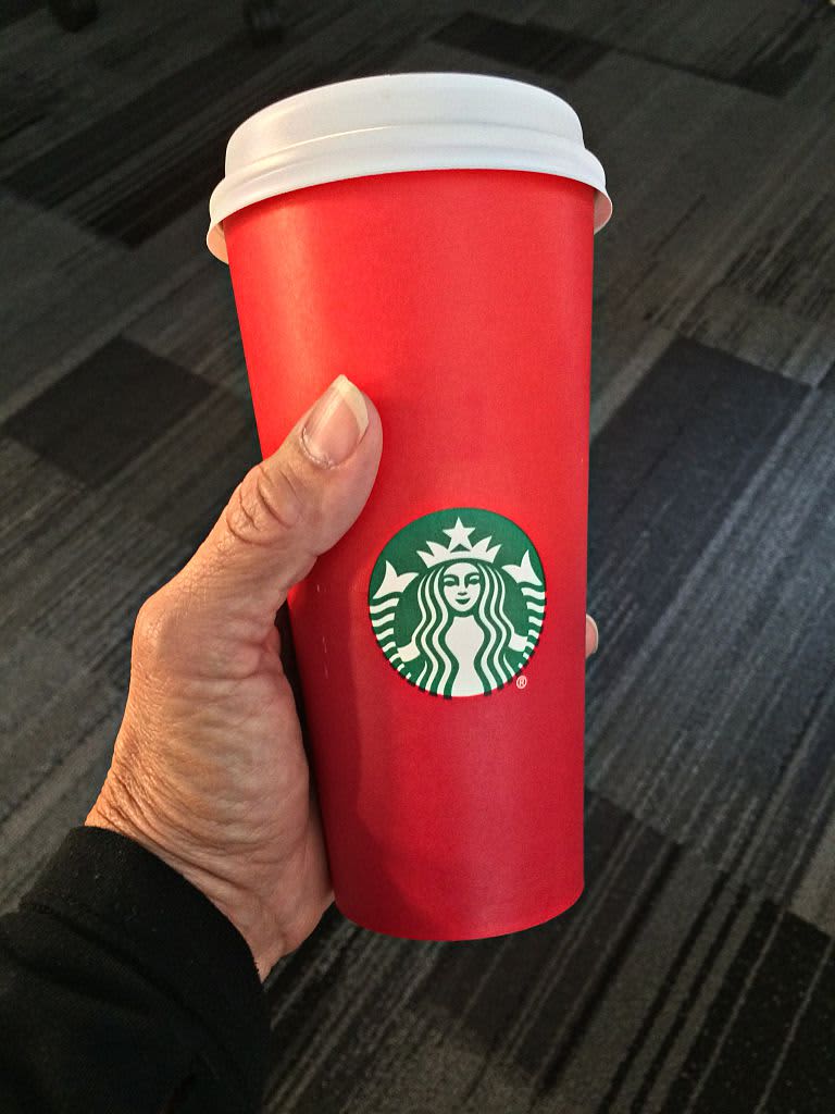 Person's hand holding a red Starbucks cup over a black and gray carpet