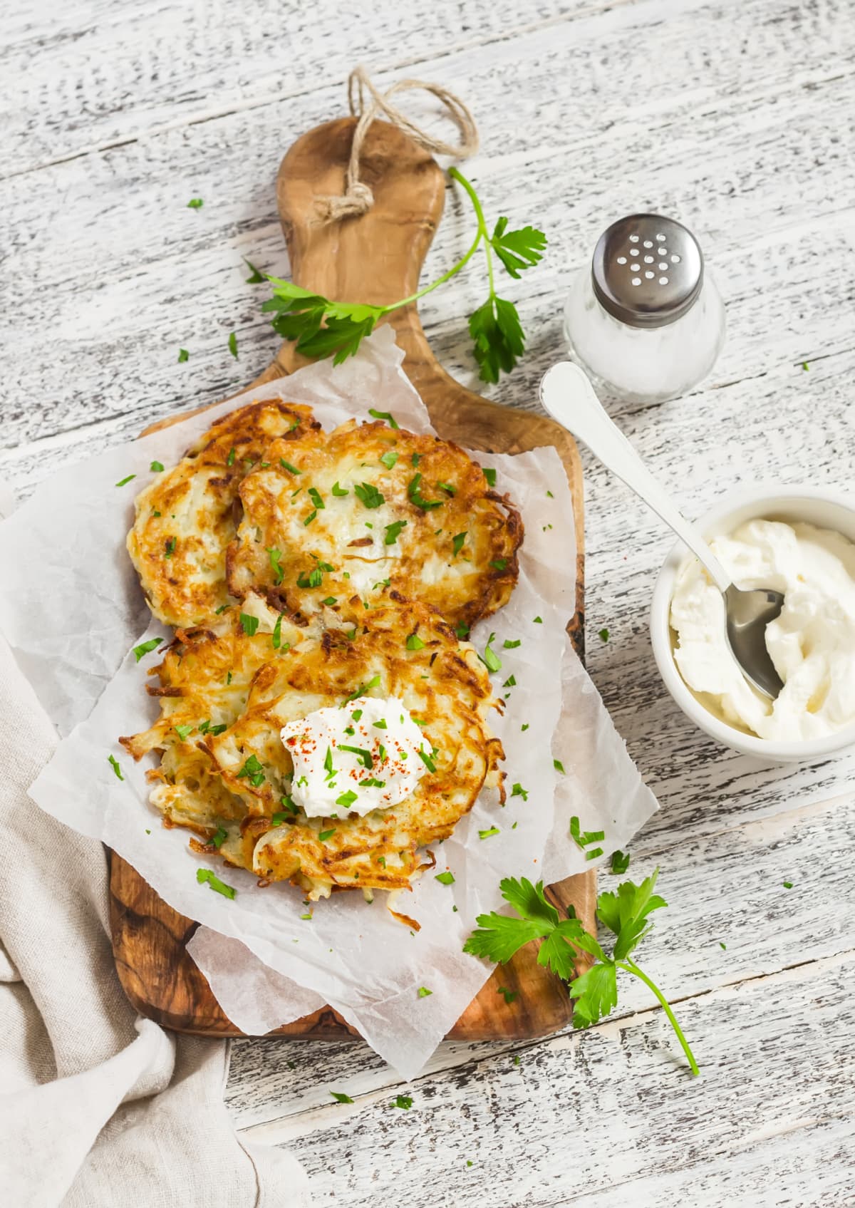 Fresh latkes topped with cilantro and sour cream on a parchment lined wooden serving board