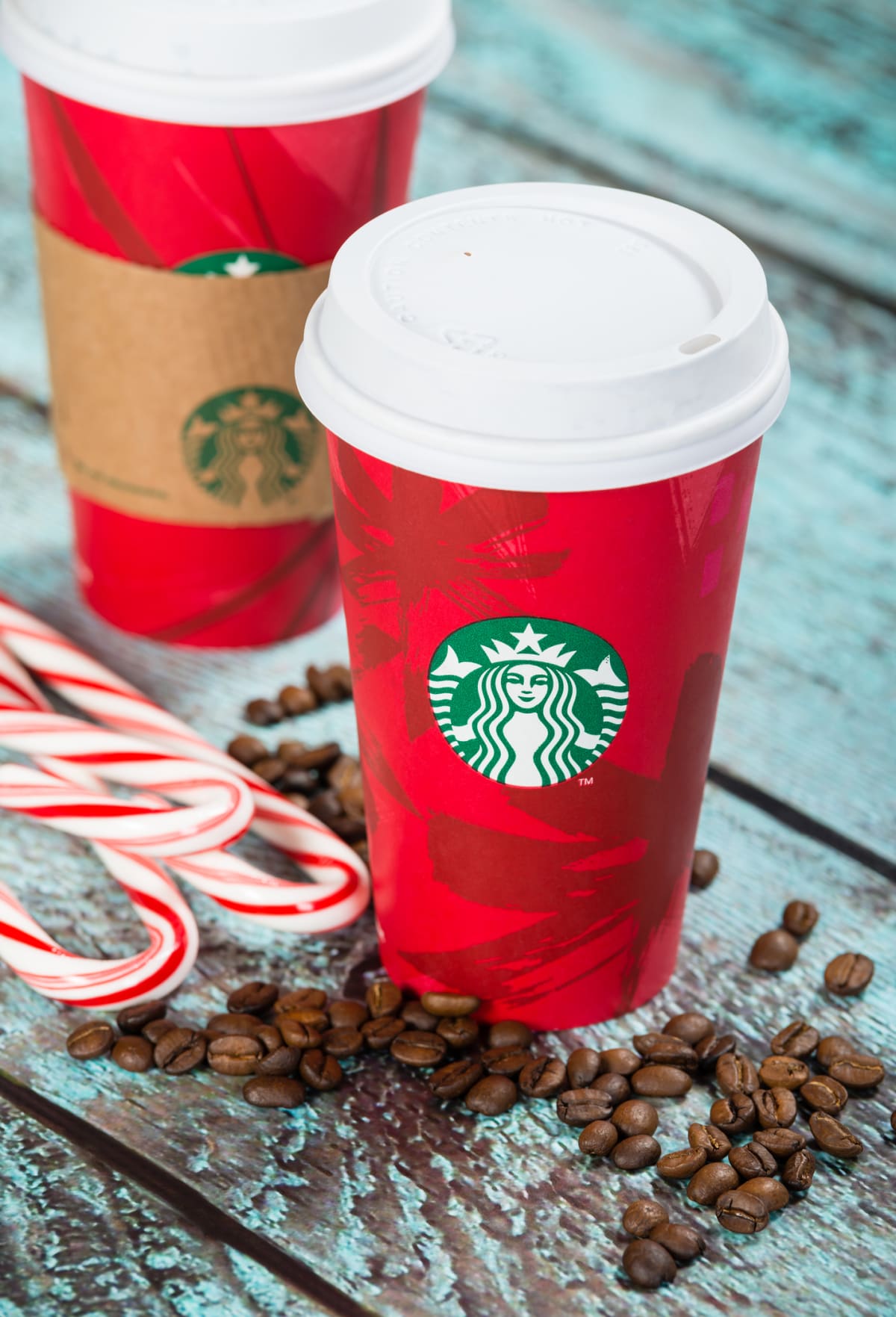 A cup of Starbucks popular holiday beverage, peppermint mocha, displayed with coffee beans and candy canes on wooden table. 