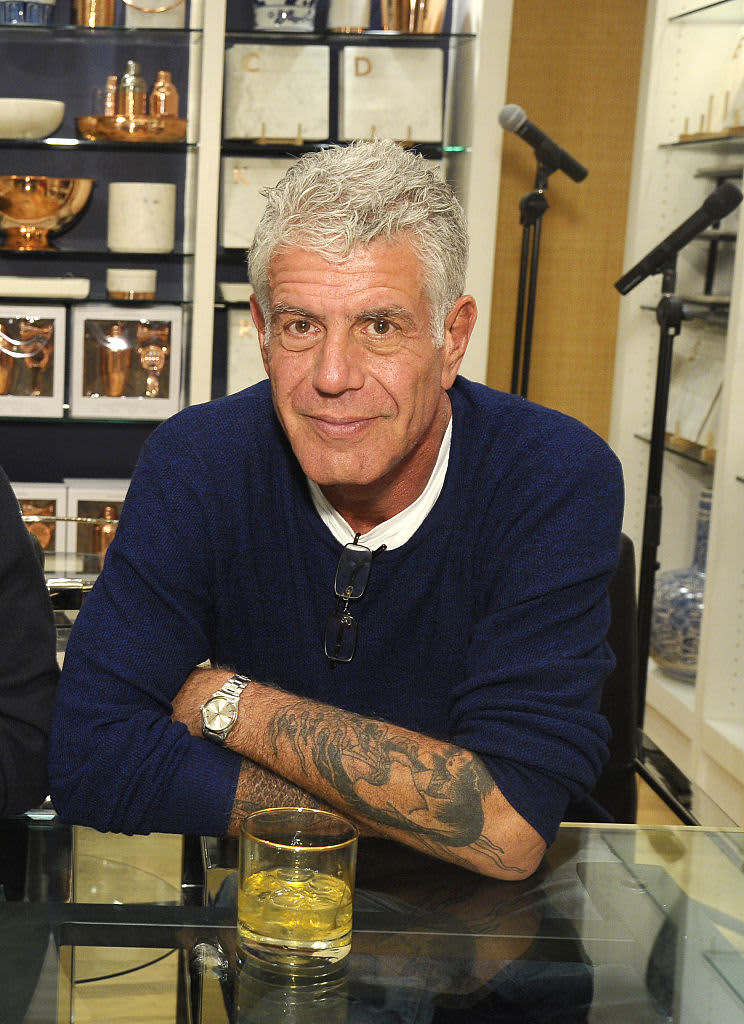 Chef Anthony Bourdain leaning against a table while seated