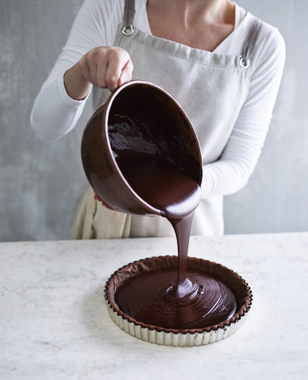 Woman pouring chocolate into a tart pan while preparing a Chocolate Ganache.