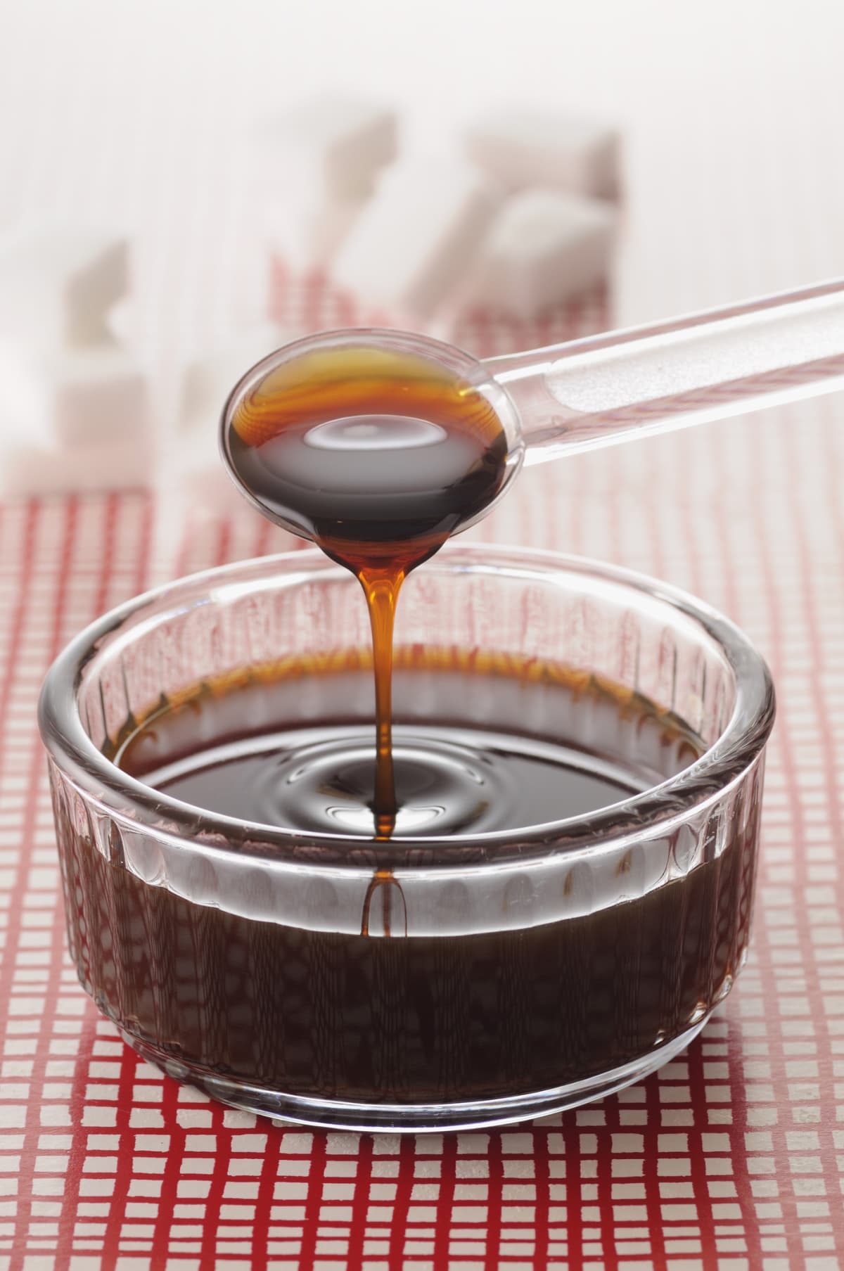 Caramel sauce pouring off a clear teaspoon into a clear bowl