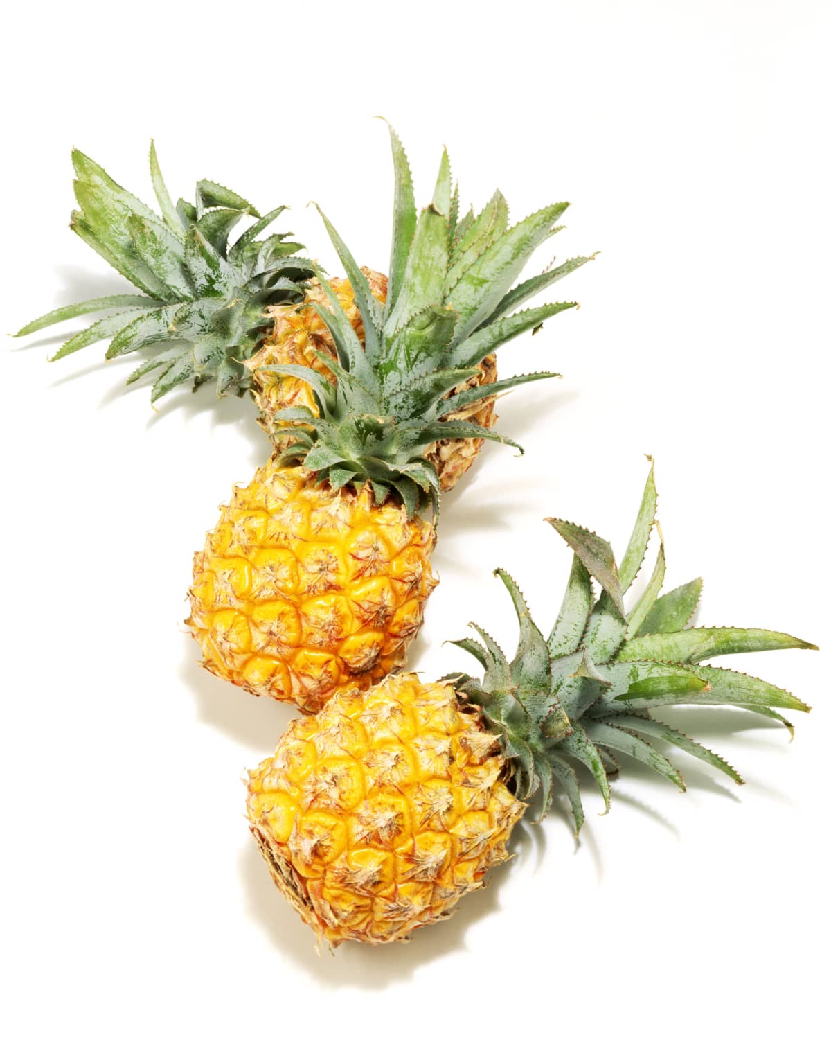 Three whole pineapples scattered on a white background