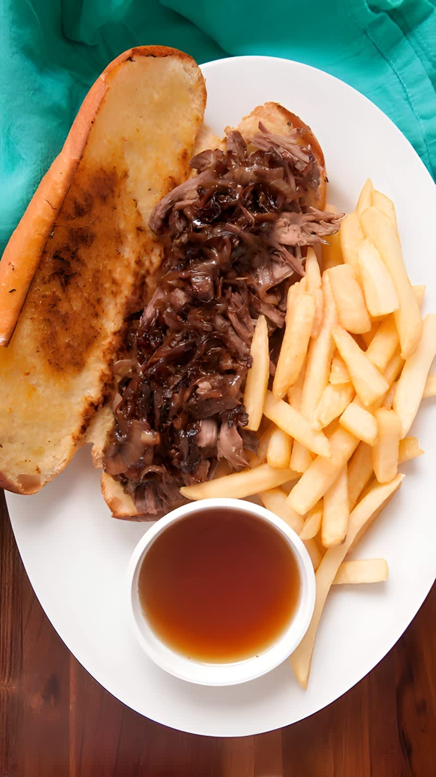 French dip sandwich on a plate with fries and dipping jus