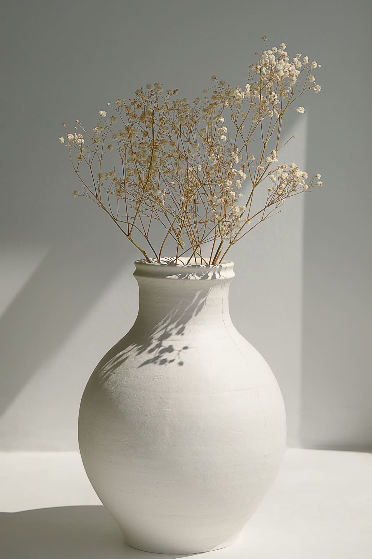 Dried flowers in a white antique vase on the window.