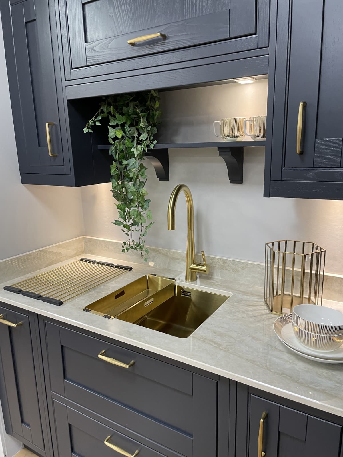 A gold sink inset in white marble kitchen counter with navy, wood grain effect cabinets above