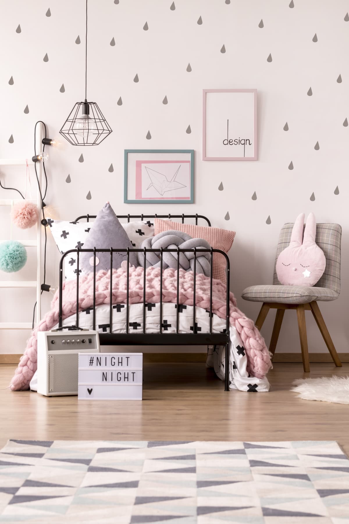 Pink knit blanket on girl's bed against the wall with posters in pastel bedroom interior with chair
