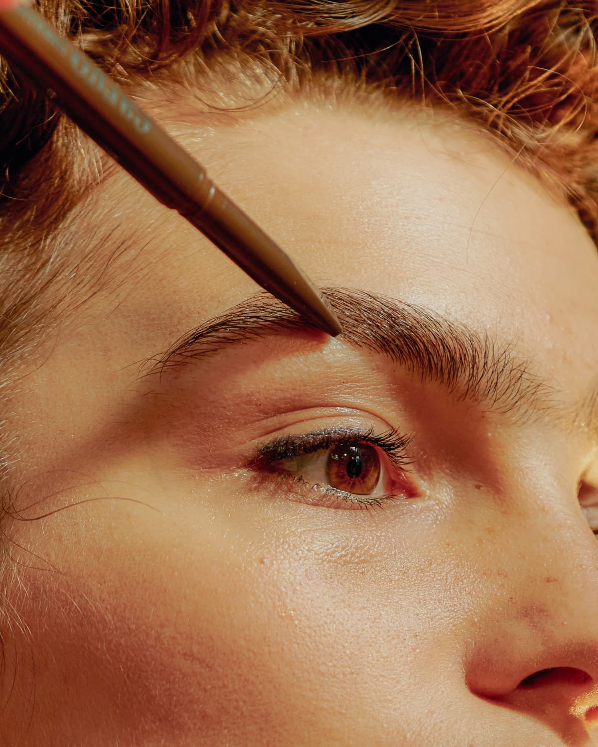 a woman filling in her eyebrows with a pencil