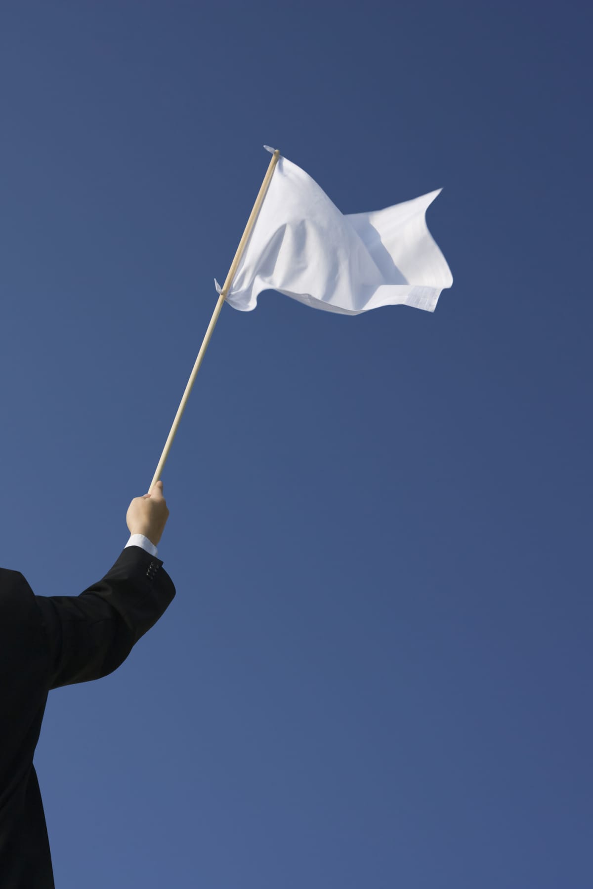 Businessman holding a white flag flutters in the wind against a blue sky.
