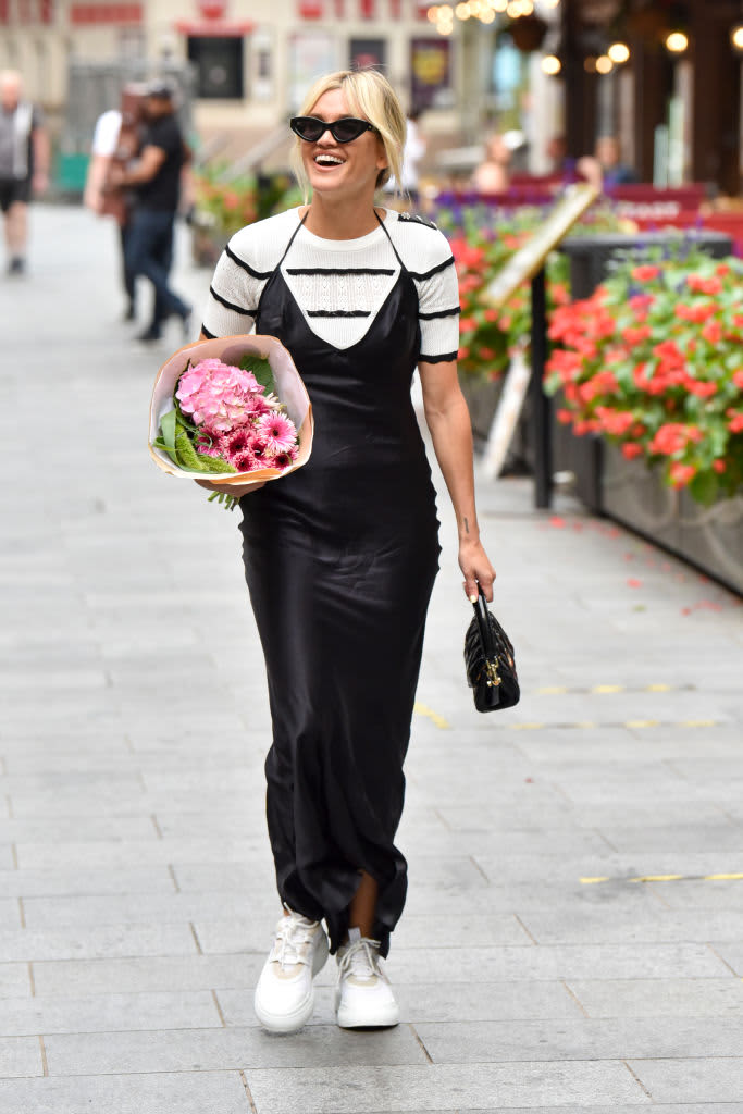 woman in black slip dress with white shirt underneath holding flowers