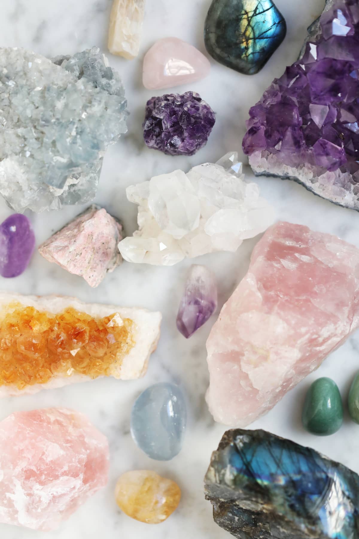 Amethyste, quartz rose, labradorite, citrine, celestine, pierre de lune, aventurine verte, rhodonite, quartz crystals on a marble countertop