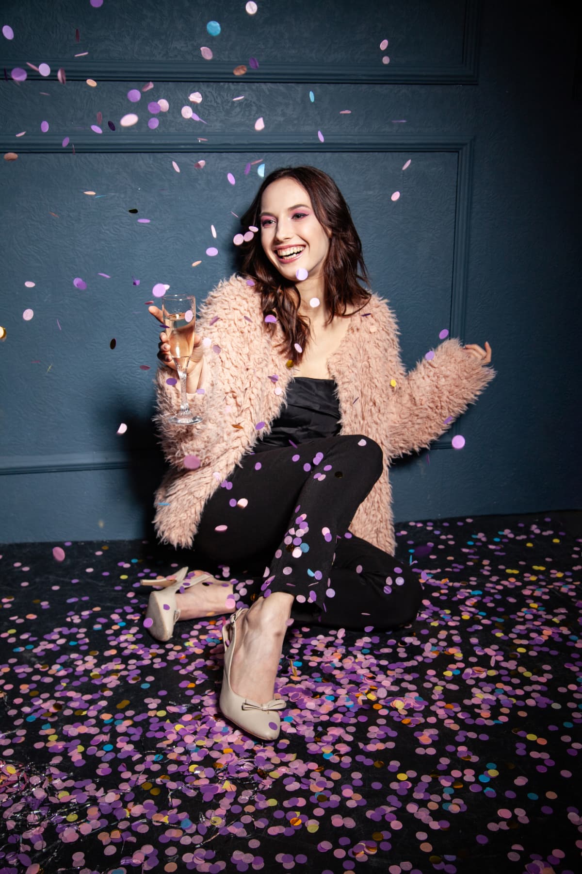 Woman throwing confetti in the air as she's seated on the floor at a party