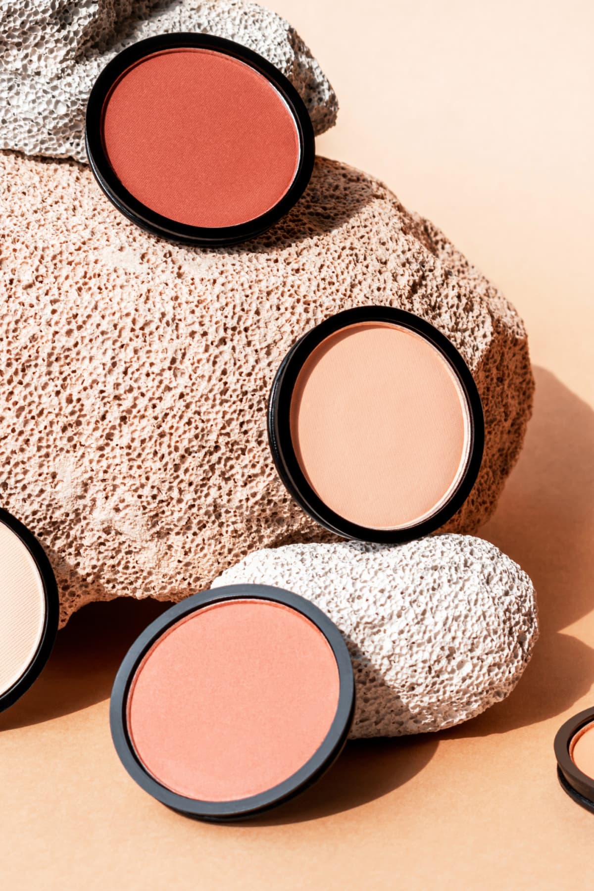 Compact face powder, blush and eyeshadow on beige background with porous stones. Vertical. Cosmetics for contouring.