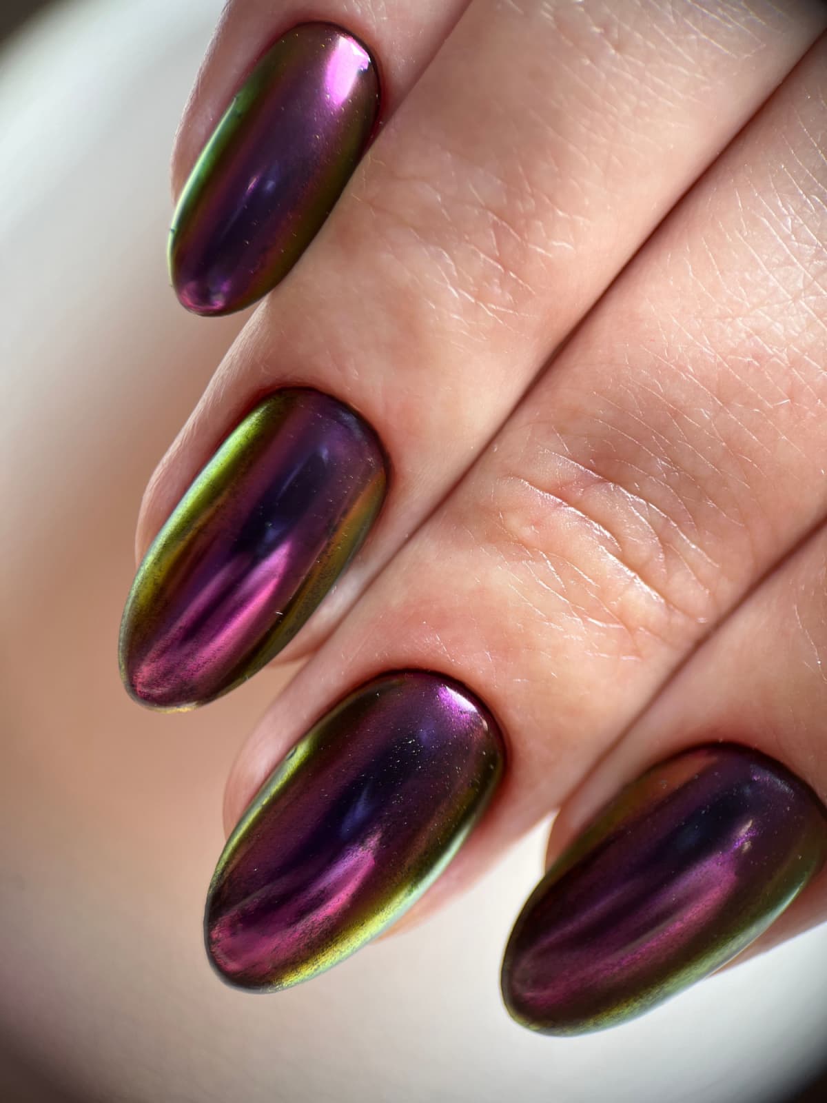 Bright iridescent gel polish with multicolored highlights. Women's hands with long almond-shaped nails and chameleon design hold a smartphone.