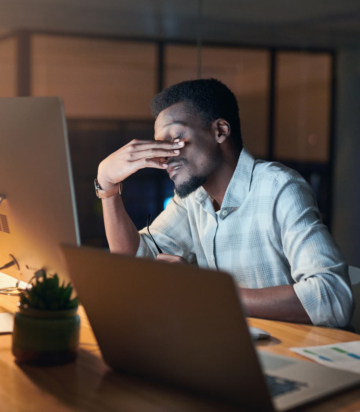 man working late at night on a laptop rubbing his eyes in frustration