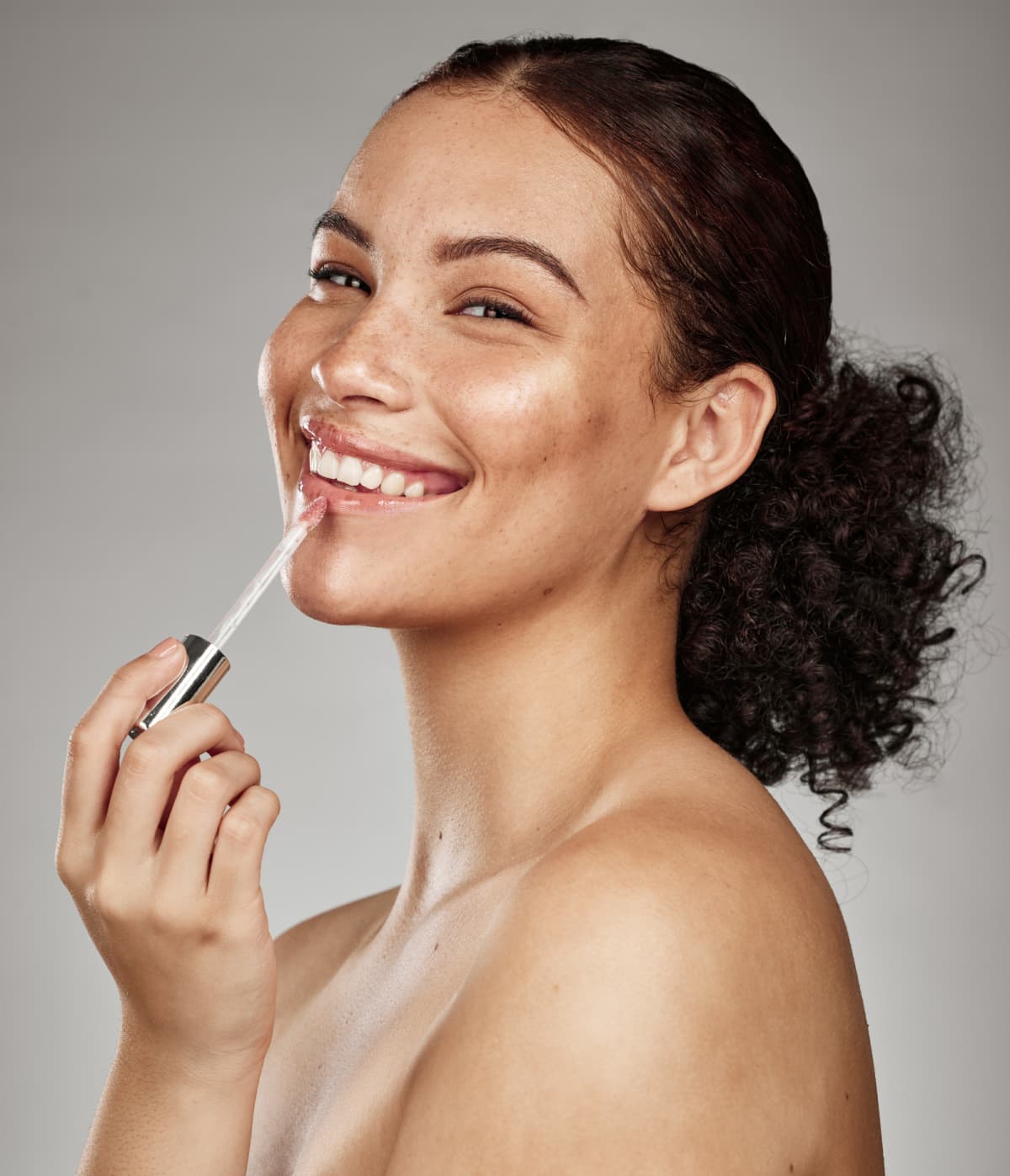 Woman, lipstick and smile for makeup cosmetics, skincare or beauty against a grey studio background. Happy female smiling with teeth in satisfaction for lip, mouth and applying cosmetic treatment
