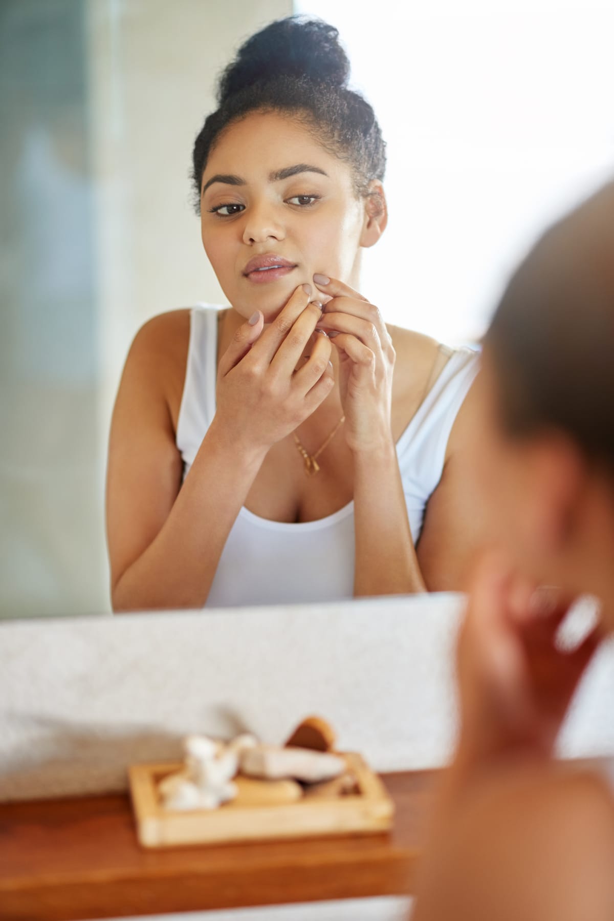 Shot of a young woman squeezing a pimple in front of the bathroom mirror