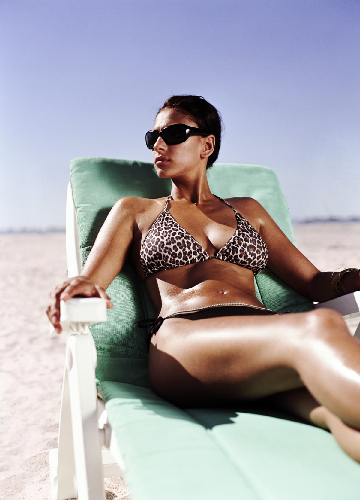 A woman sits in a beach chair in a bikini and sunglasses