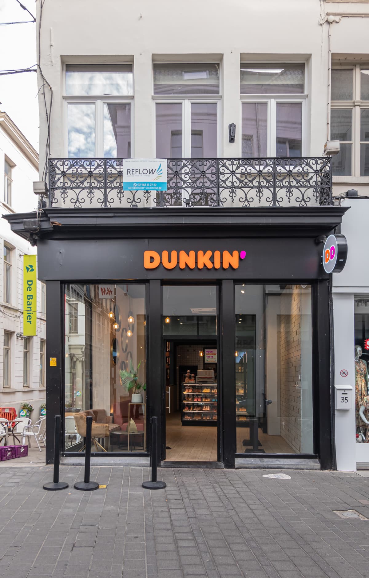 Gent, Flanders, Belgium - July 30, 2021: Dunkin Donuts store black and window facade on corner showing display inside and advertising as DD.