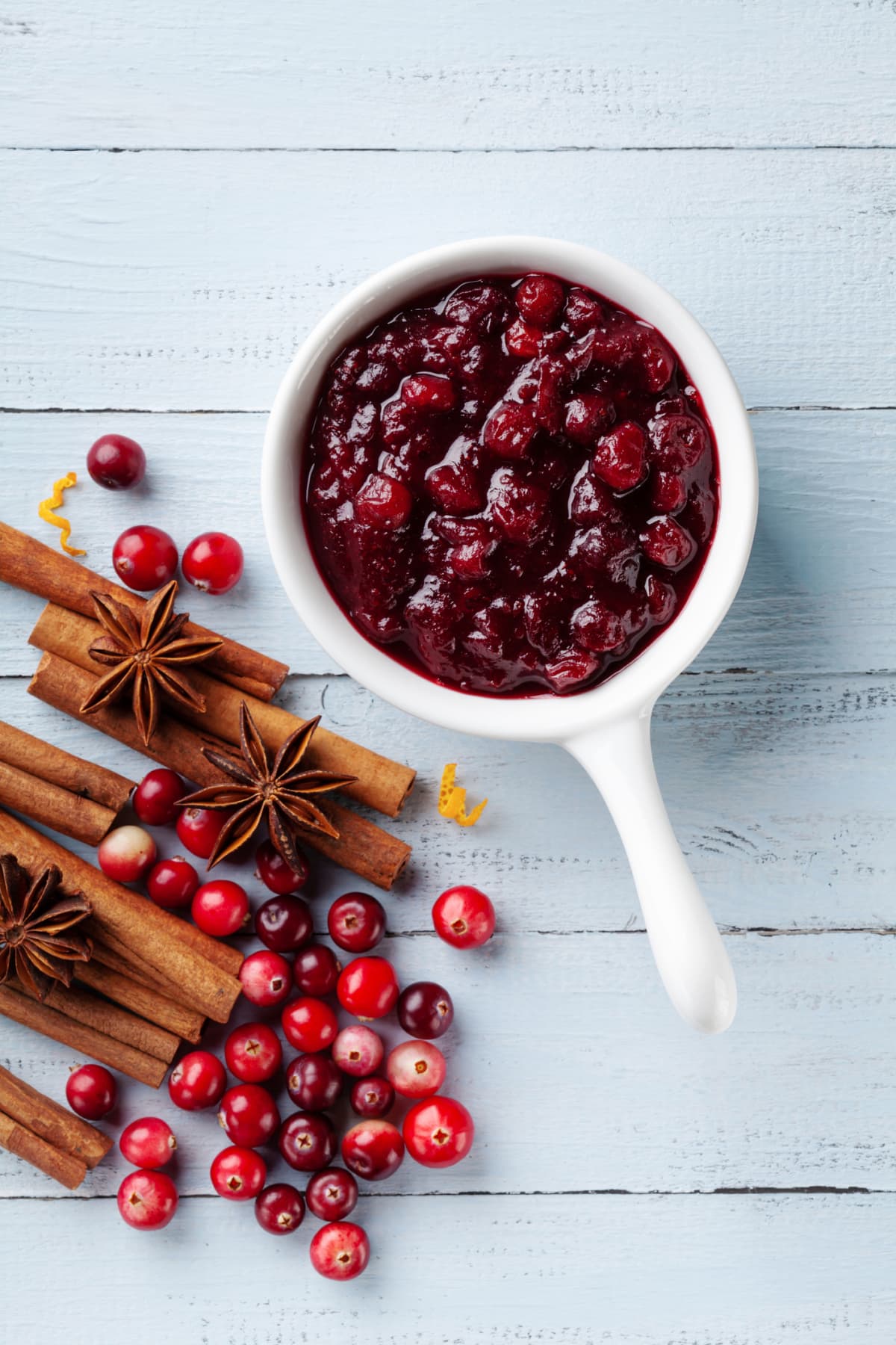 Cranberry sauce in white ceramic dish with ingredients for cooking on blue wooden table top view and vertical.