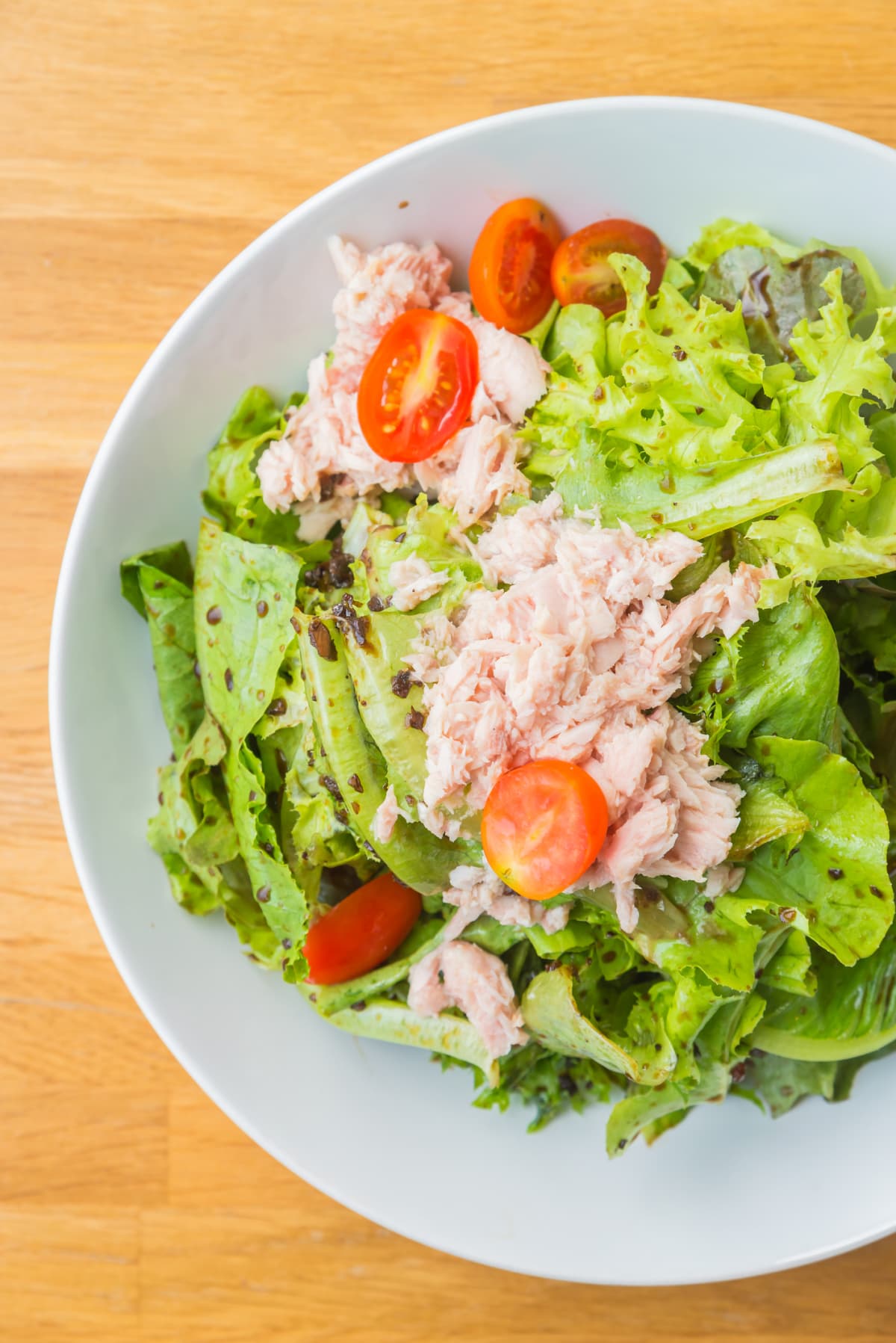A tuna salad on a bed of green salad with tomatoes