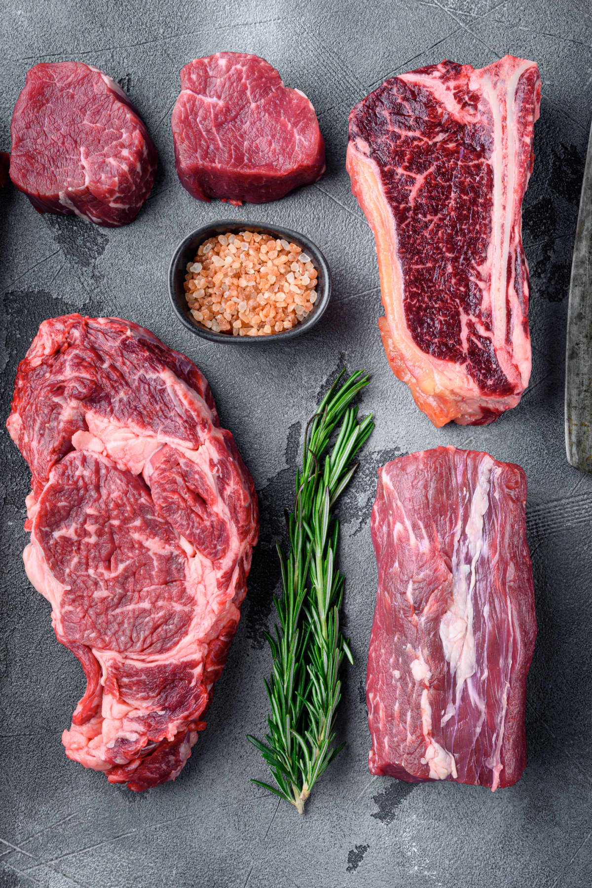 Variety of Raw Black Angus Prime meat steaks set, tomahawk, t bone, club steak, rib eye and tenderloin cuts, on gray stone background.