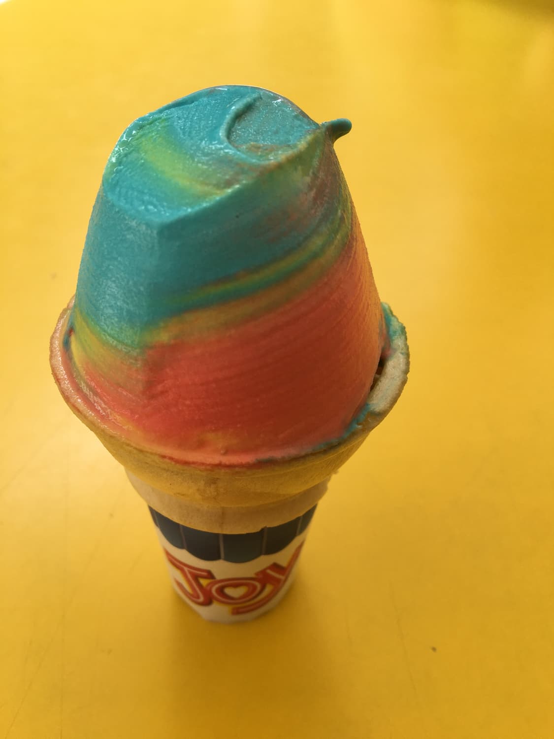 superman ice cream in a cone. pink, yellow and blue colored ice cream cone sitting on a yellow background